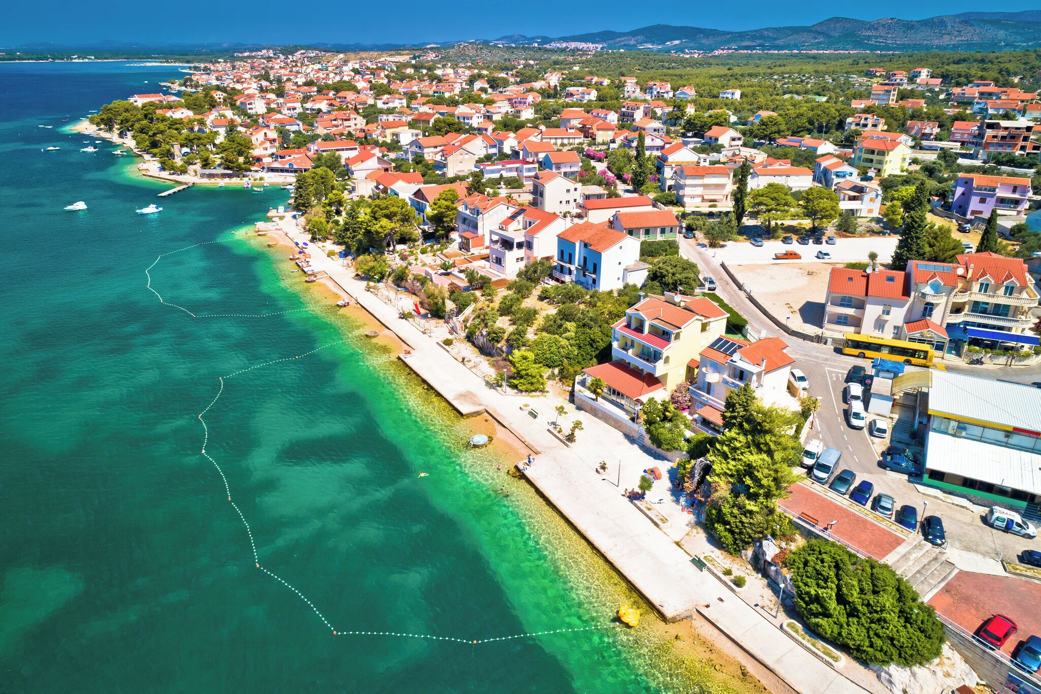 Eine Vogelperspektive einer Küstenstadt mit Wohngebäuden, einem Strand und klarem Wasser.