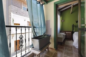 Une pièce avec un lit, une petite table sur laquelle est posée une plante, une fenêtre avec un rideau et un mur vert.