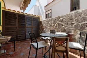 A patio with a round table and chairs, a stone wall, and a window with shutters. - Quiet house by the sea / beach, WiFi, child-friendly, terrace - great location (Alcalá)