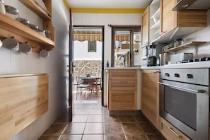 A narrow kitchen with wooden cabinets, a built-in oven, and a dining area visible through an open door. - Quiet house by the sea / beach, WiFi, child-friendly, terrace - great location (Alcalá)