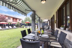 Un patio exterior con una mesa lista para comer, rodeado de sillas y una zona cubierta con sombrillas.