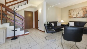 Ein Wohnzimmer mit Treppe, einem schwarzen Ledersessel, einer schwarzen Couch und einem Wandbild.