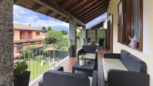 Ein überdachter Balkon mit Korbmöbeln, Blick auf den Garten und ein Gebäude im Hintergrund.