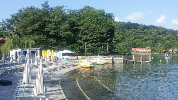 Eine Uferpromenade am See mit Booten, Liegestühlen und Sonnenschirmen.
