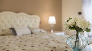 Ein Bett mit einem Punkte-Muster-Überwurf, eine Vase mit weißen Blumen und eine Nachttischlampe.