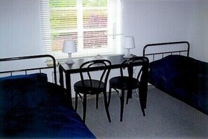 A room with two single beds, a small table with a lamp, and a chair.