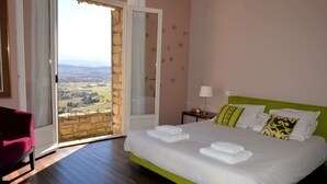 Une chambre avec un lit vert, du linge de lit blanc, une vue à travers une porte vitrée et une chaise rouge.