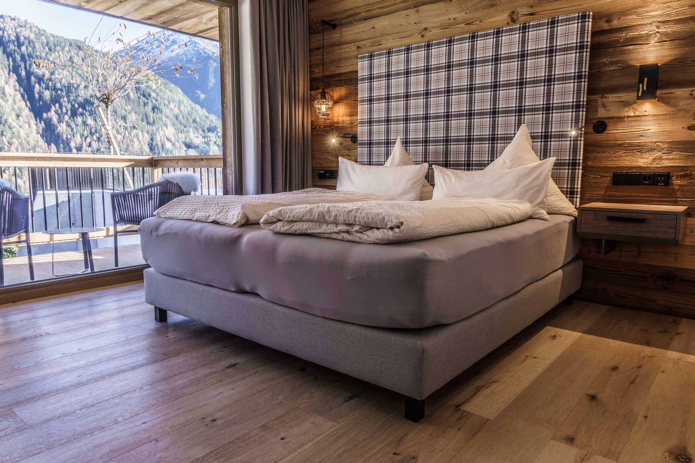 Een slaapkamer met een groot bed, houten wanden, een ruitjes hoofdeinde en een balkon met uitzicht op de bergen.
