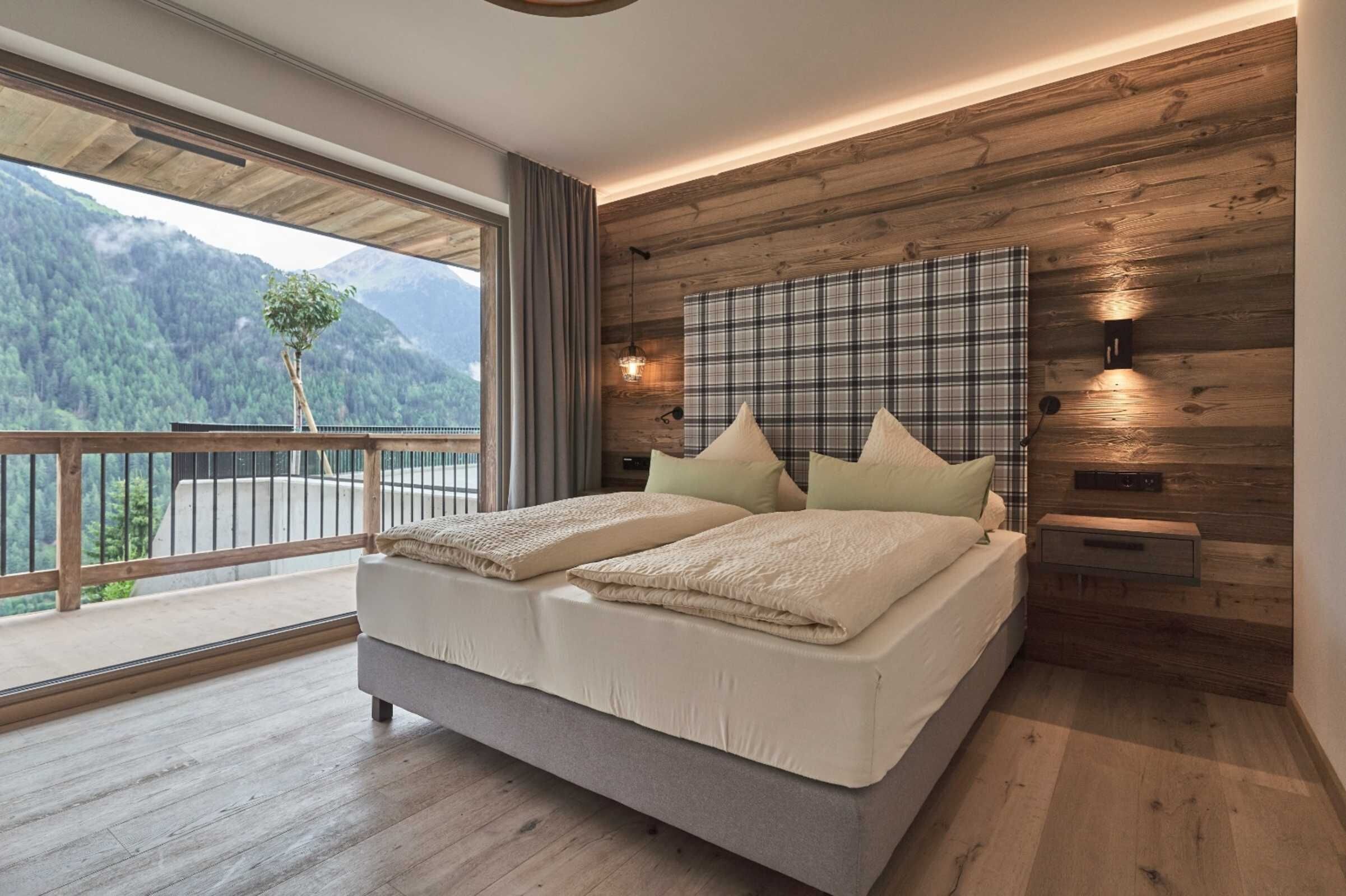 A bedroom with a large bed, wooden panel walls, a view of mountains, and a balcony.