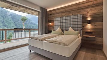 A bedroom with a large bed, wooden panel walls, a view of mountains, and a balcony.