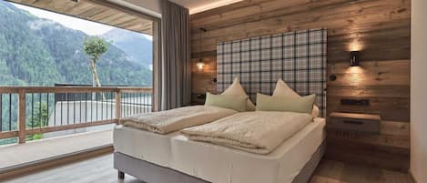 Ein Schlafzimmer mit einem großen Bett, Holzwandverkleidung, Blick auf Berge und einem Balkon.