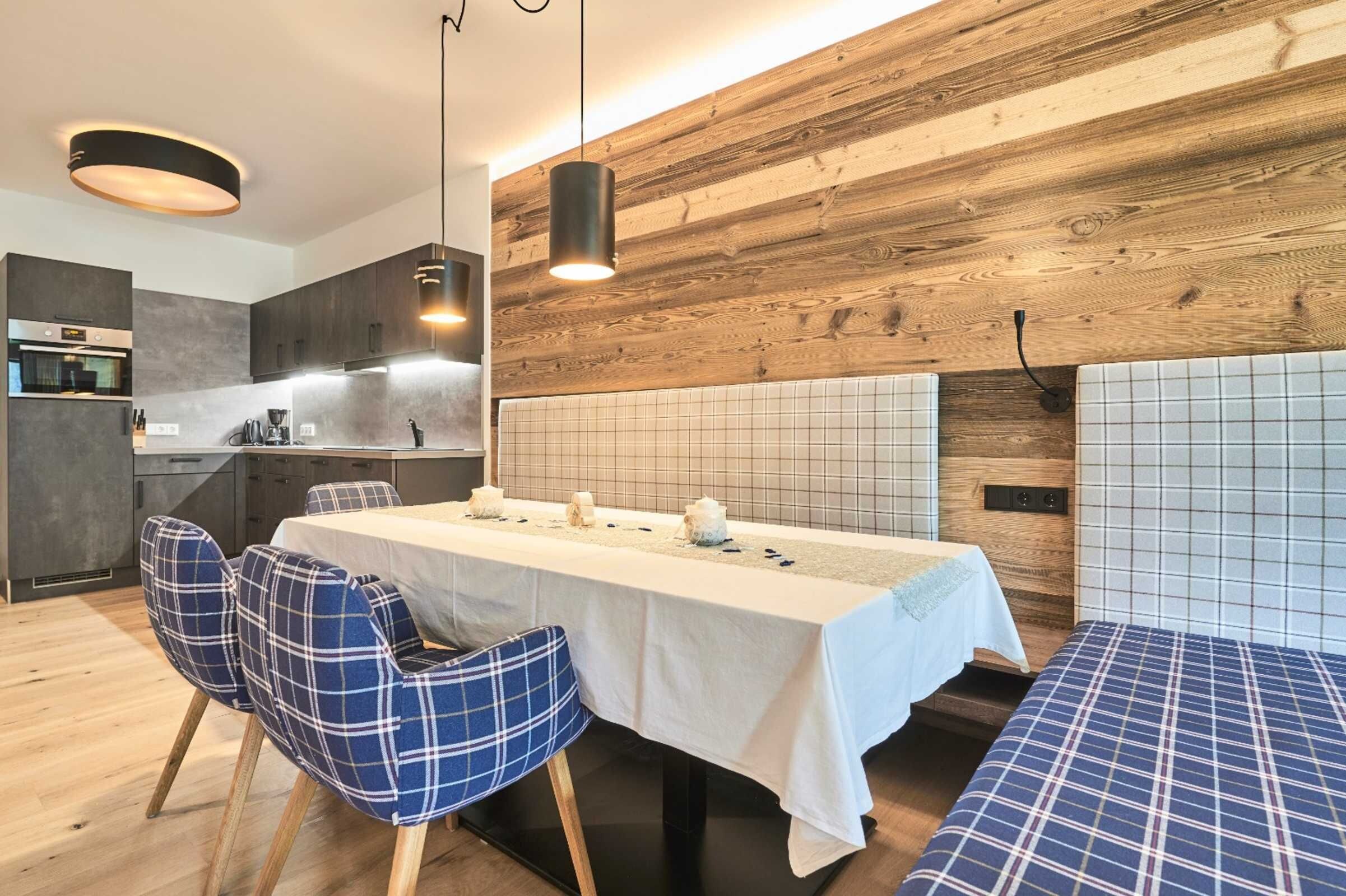 A modern kitchen with wooden accents, a dining area with a long table and blue chairs, and a bench with a checkered pattern.