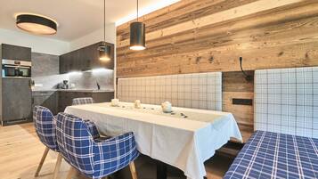 A modern kitchen with wooden accents, a dining area with a long table and blue chairs, and a bench with a checkered pattern.