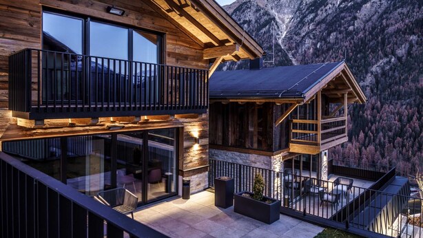 Une cabane moderne en bois, dotée d’un balcon, de grandes fenêtres et offrant une vue sur les montagnes.