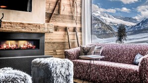 Une pièce chaleureuse avec une cheminée, un canapé et une vue sur des montagnes enneigées.