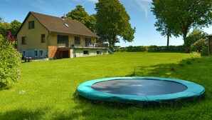 Een huis met een groot gazon en een trampoline op de voorgrond.