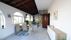 Ruime kamer met een hoge plafond, een zithoek met stoelen en een tafel, en een receptiebalie met een plant.