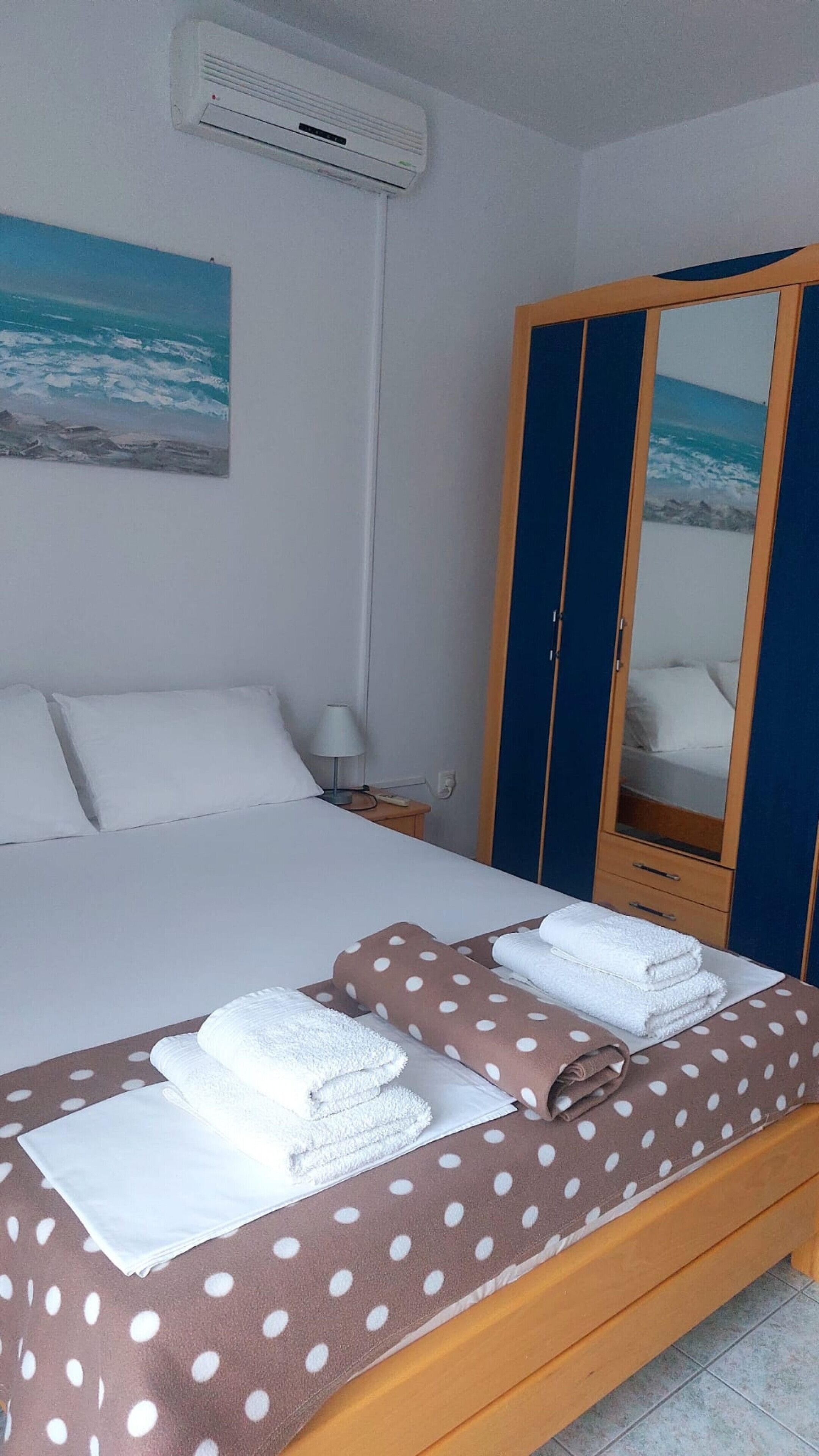 Una habitación de hotel con una cama, un armario, una mesita de noche y un cuadro marino en la pared.