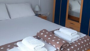A hotel room with a bed, a wardrobe, a nightstand, and a painting of the sea on the wall.