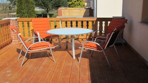 Eine Holzterrasse mit einem runden Tisch und vier orangefarbenen Stühlen.
