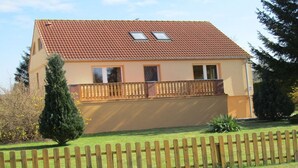 Ein zweistöckiges Haus mit rotem Ziegeldach, einem Balkon mit Holzgeländer und einem kleinen Garten.