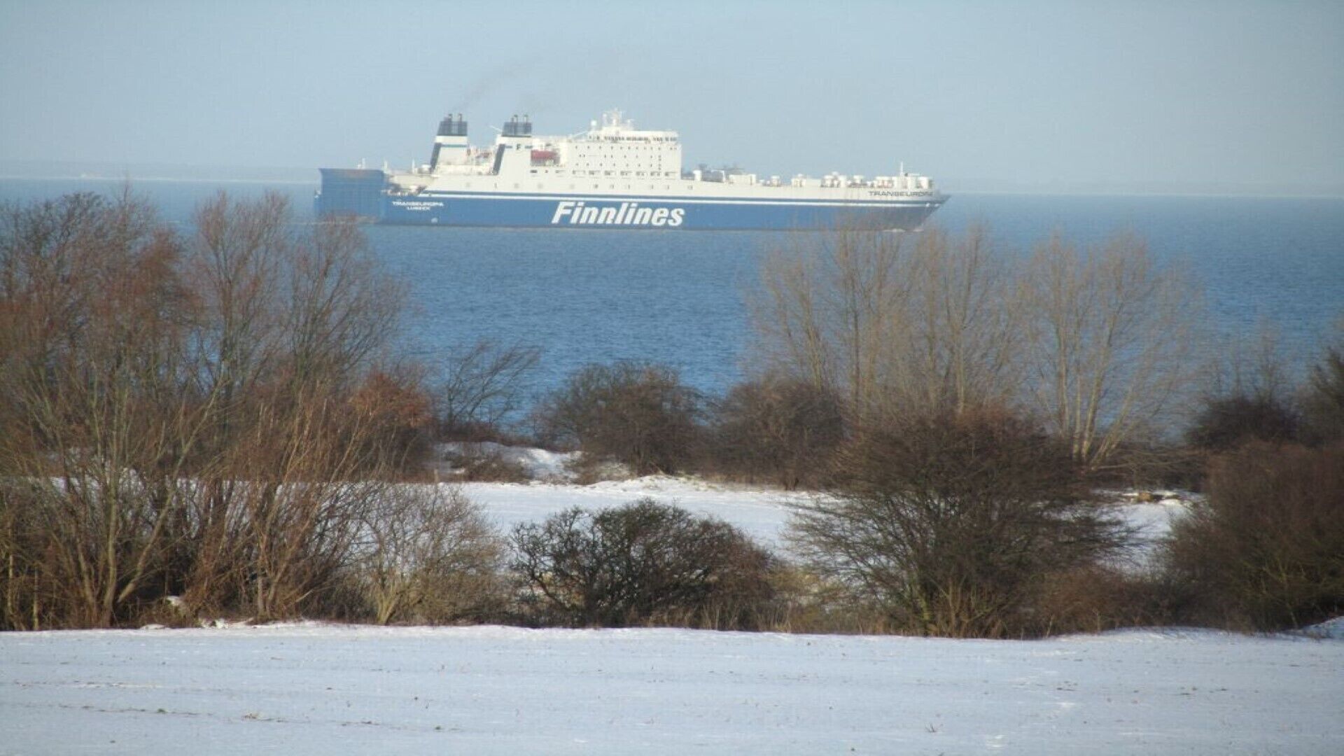 Un grand navire portant le nom « Finnlines » sur sa coque était amarré dans un port. Au premier plan, on pouvait voir un paysage enneigé et des arbres.