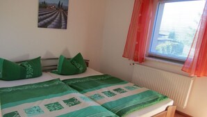 Ein Schlafzimmer mit einem Bett, grüner Bettwäsche, einem Fenster mit roten Vorhängen und einem Bild an der Wand.