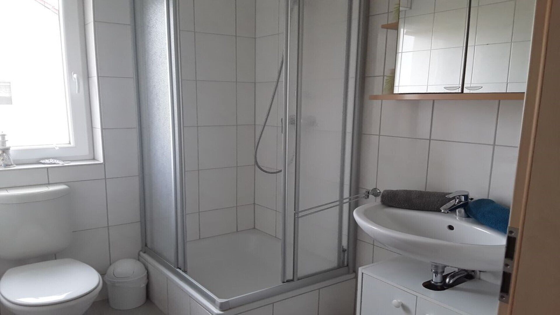 Een badkamer met douche, toilet, wastafel en een raam.