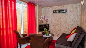 A living room with a brown sofa, two brown chairs, a red curtain, a television, and a small table with a plant. - la cariole (Saint-Pierre)