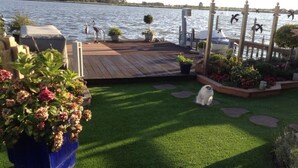 A deck with artificial grass, potted plants, and a white dog. - Luxurious holiday home directly on the lake (Wervershoof)