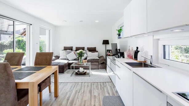 Eine moderne Wohnung mit Essbereich, Sofagarnitur, Küche und großen Fenstern.