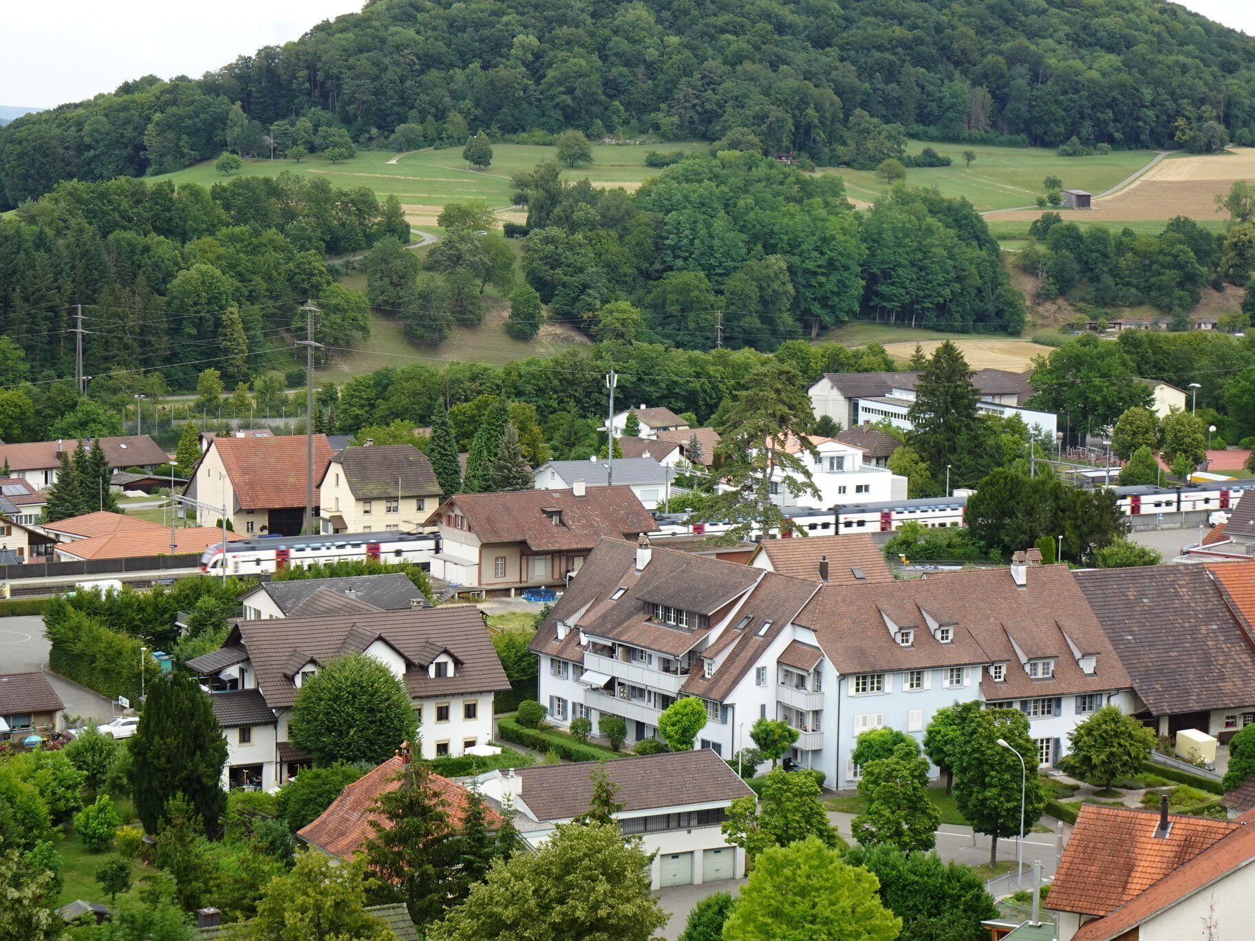 Ein Wohngebiet mit Häusern, einem Zug und einer hügeligen Landschaft im Hintergrund.