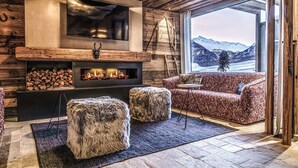 A cozy living room with a fireplace, a TV mounted on the wall, and a view of snow-capped mountains. - Vacation apartment Melisande 3 - The Peak Sölden (Sölden)