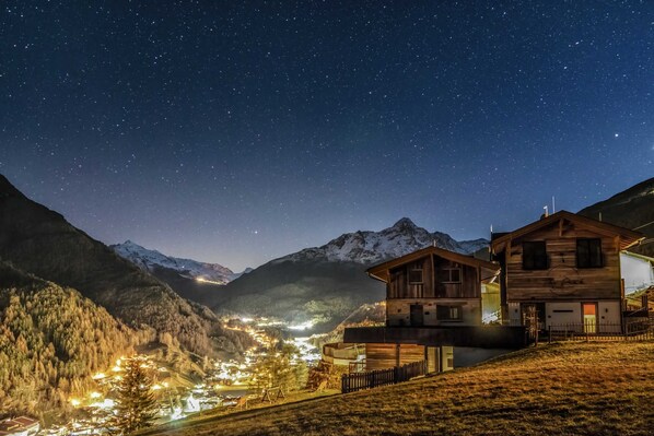 Un village de montagne la nuit, avec des bâtiments illuminés et un ciel étoilé.