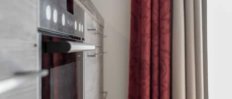 A kitchen with an oven and a microwave, a window with curtains, and a door.