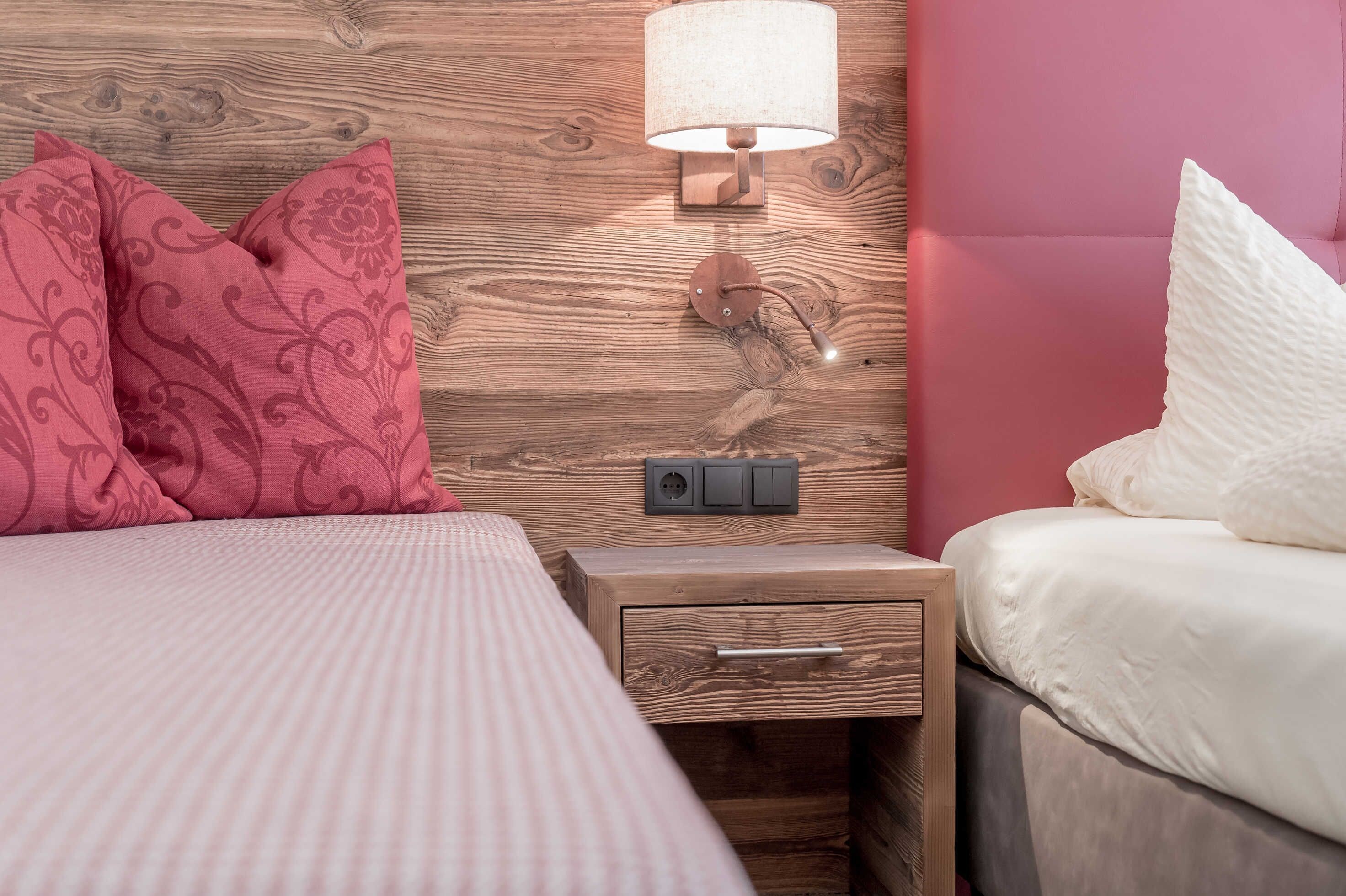 Une chambre à coucher avec une tête de lit en bois, une lampe de chevet, une table de chevet avec un tiroir et un lit avec une literie rose et blanche.