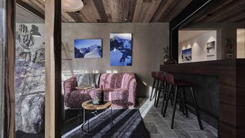 A modern interior with a wooden ceiling, a pink patterned sofa, a small round table, and a bar area with stools.