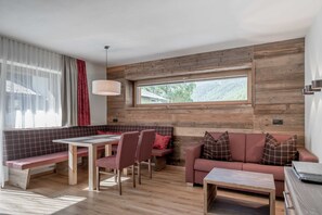 A modern interior with a wooden wall, a dining area with a bench and chairs, a sofa, and a large window.