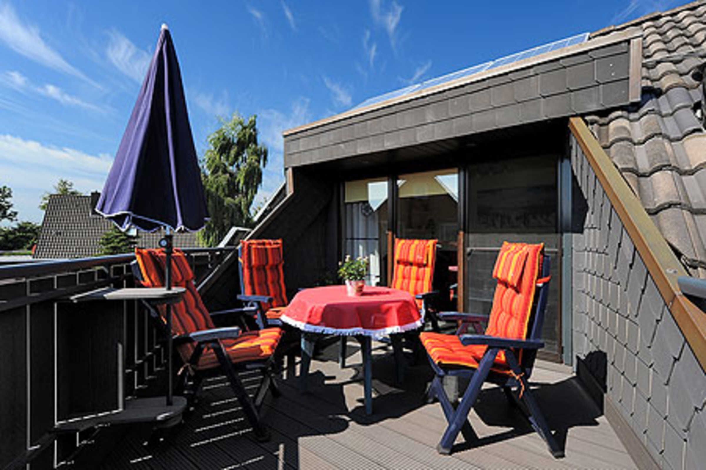 Un patio al aire libre con una mesa y sillas, un paraguas azul y vistas a un edificio con tejado de baldosas.