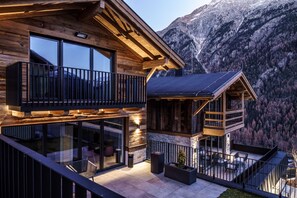 A modern wooden cabin with a balcony, large windows, and a mountain backdrop.
