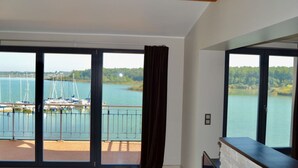 Amplia habitación con grandes puertas correderas de vidrio que dan a un balcón con vista a un puerto deportivo y un lago.