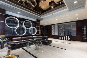 A modern living room with a sectional sofa, a glass coffee table, and decorative circular mirrors on the wall. - Hotel Sandy's Tower (Bhubaneshwar)