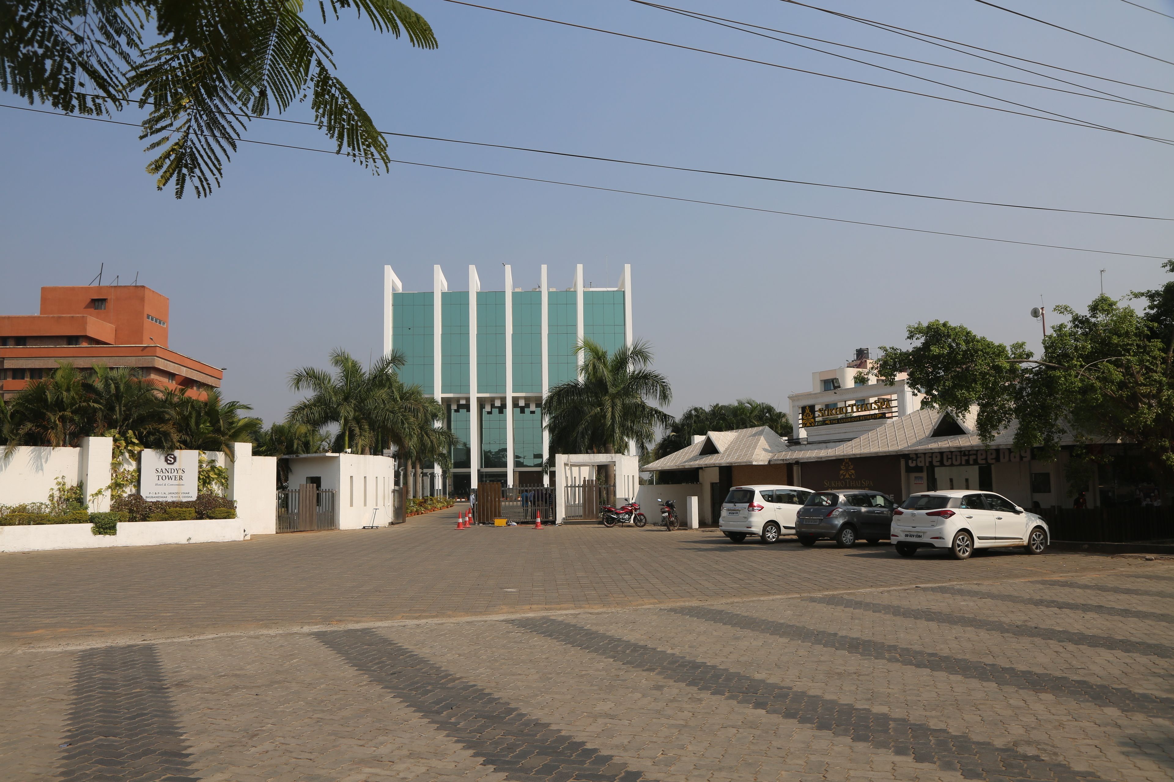 A parking area with several cars, a building with a sign reading "SANDY'S TOWER," and a cafe named "Cafe Coffee Day."