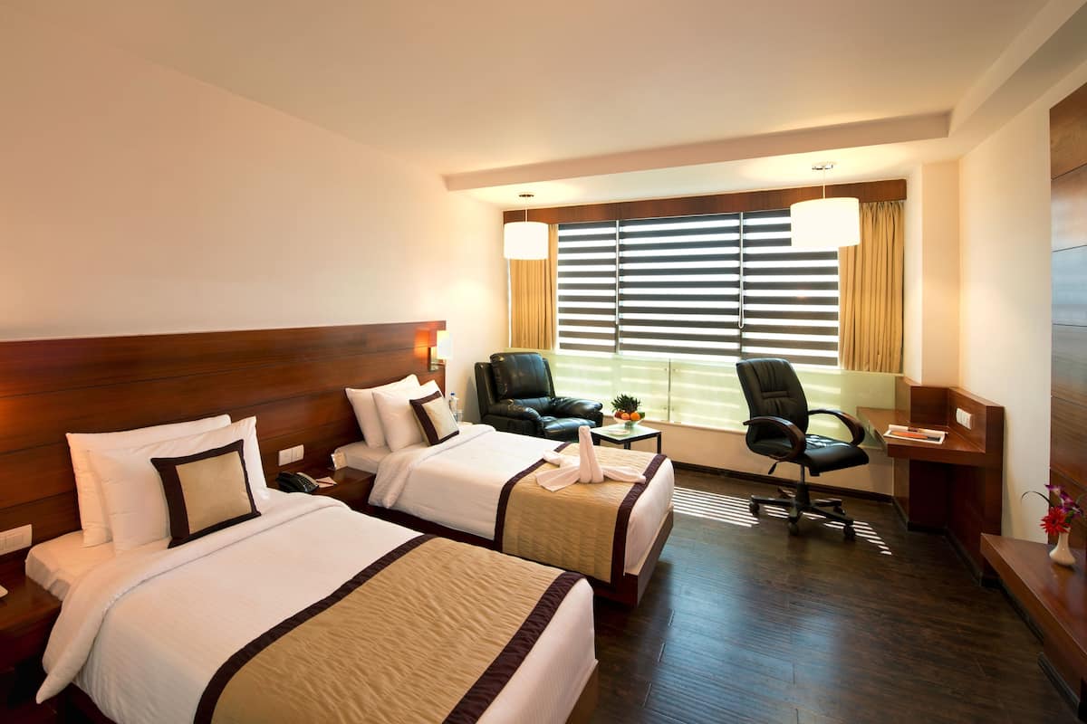 Habitación de hotel con dos camas, un escritorio, una silla y una ventana con persianas.