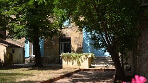 Un camino que lleva a un edificio de piedra con puerta azul, rodeado de follaje y un cielo despejado.