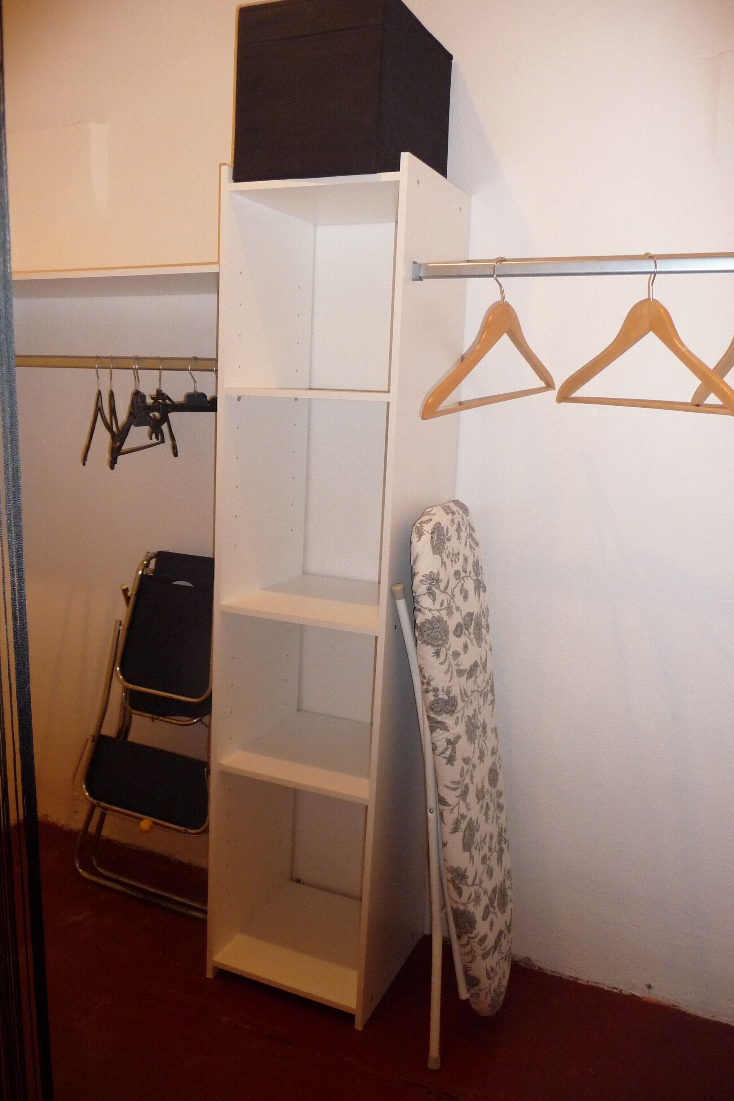 Una habitación con un armario blanco, una tabla de planchar negra y un perchero de madera.