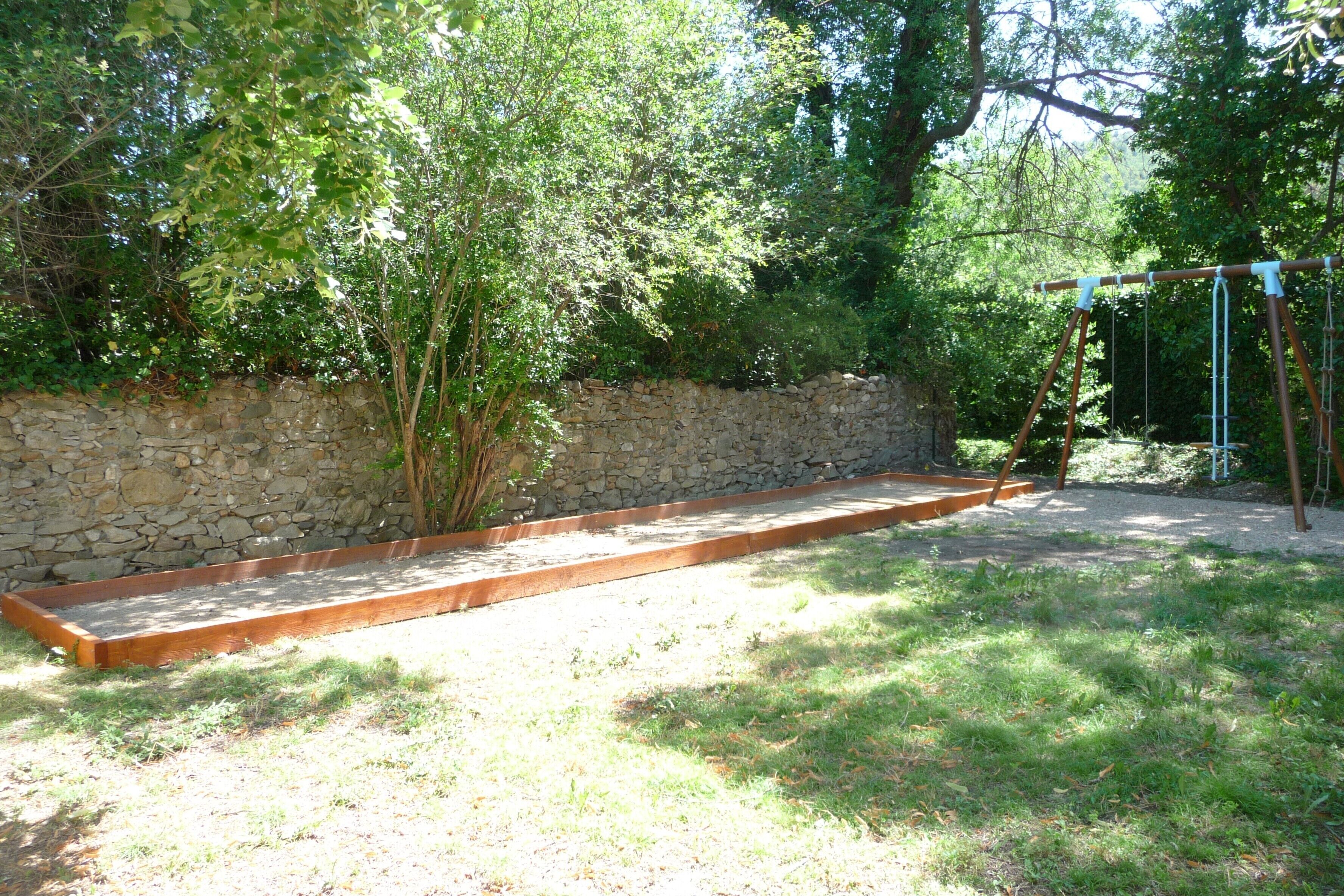 Eine Steinsichtmauer, eine Holzbank und eine Schaukel im Garten.
