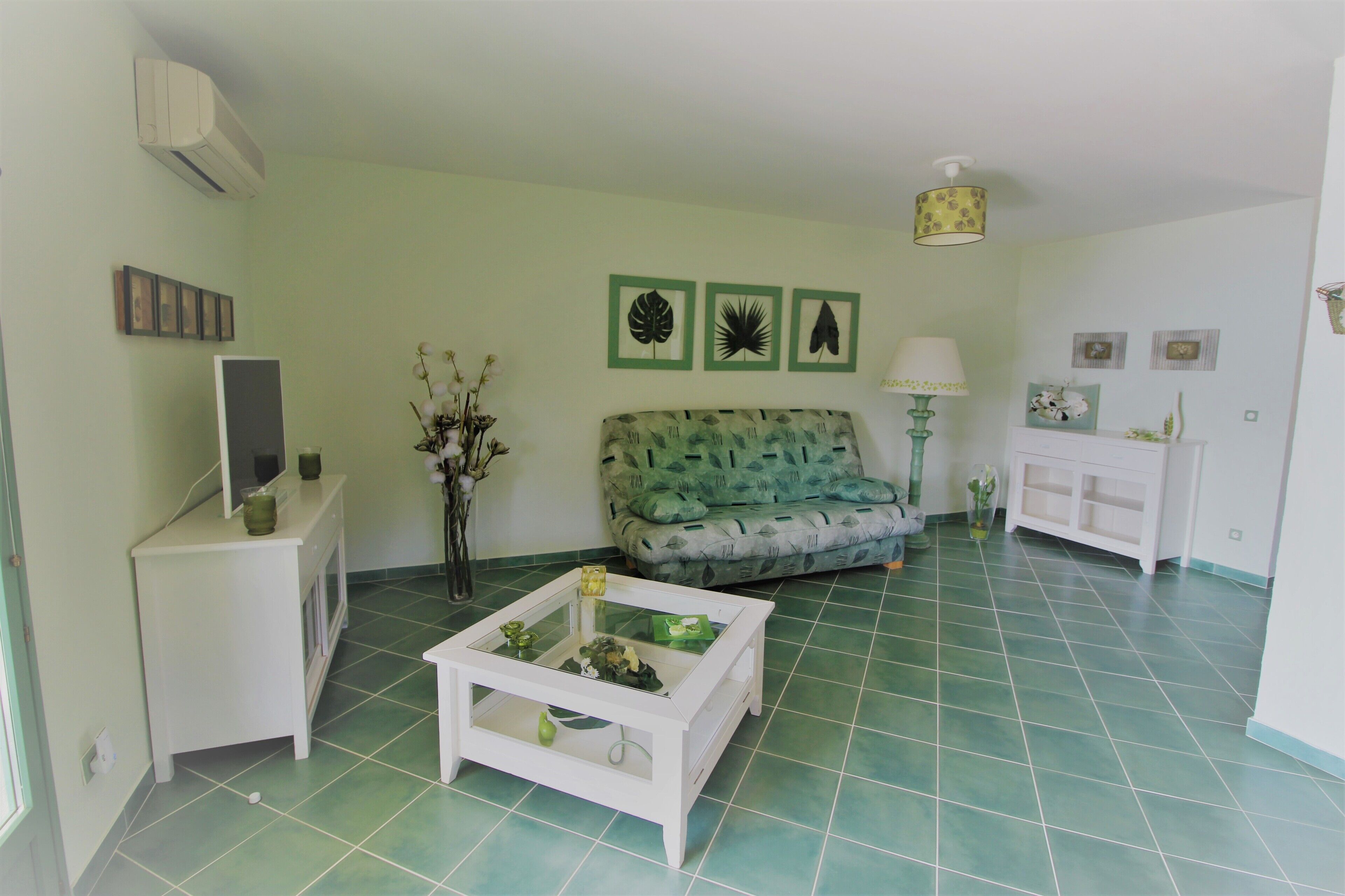Un salon avec un canapé vert, une table basse blanche et un téléviseur posé sur un meuble blanc.