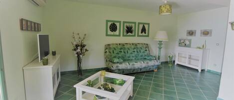 Un salon avec un canapé vert, une table basse blanche et un téléviseur posé sur un meuble blanc.