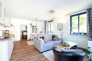 A modern living room with a grey sofa, a black leather chair, and a dining area with a white table and chairs.